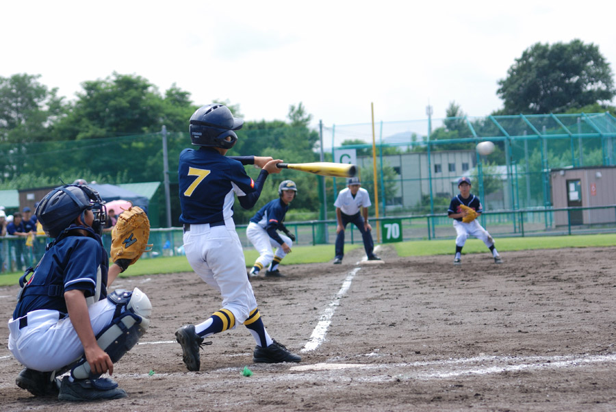 少年野球の試合でバットを振る子どもと、キャッチャー・審判